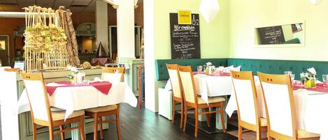 Un ristorante con sedie e tavoli di legno, un menu alla lavagna e una struttura decorativa con piante.