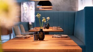 A restaurant interior with wooden tables, blue cushioned seating, and hanging pendant lights. - Golden Leaf Parkhotel Im Lehel (Munich)