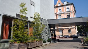 A building with a stone facade, a modern entrance, and a traditional building in the background. - Golden Leaf Parkhotel Im Lehel (Munich)