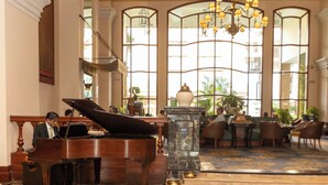 A grand lobby with a grand piano, marble flooring, and large arched windows with a chandelier.