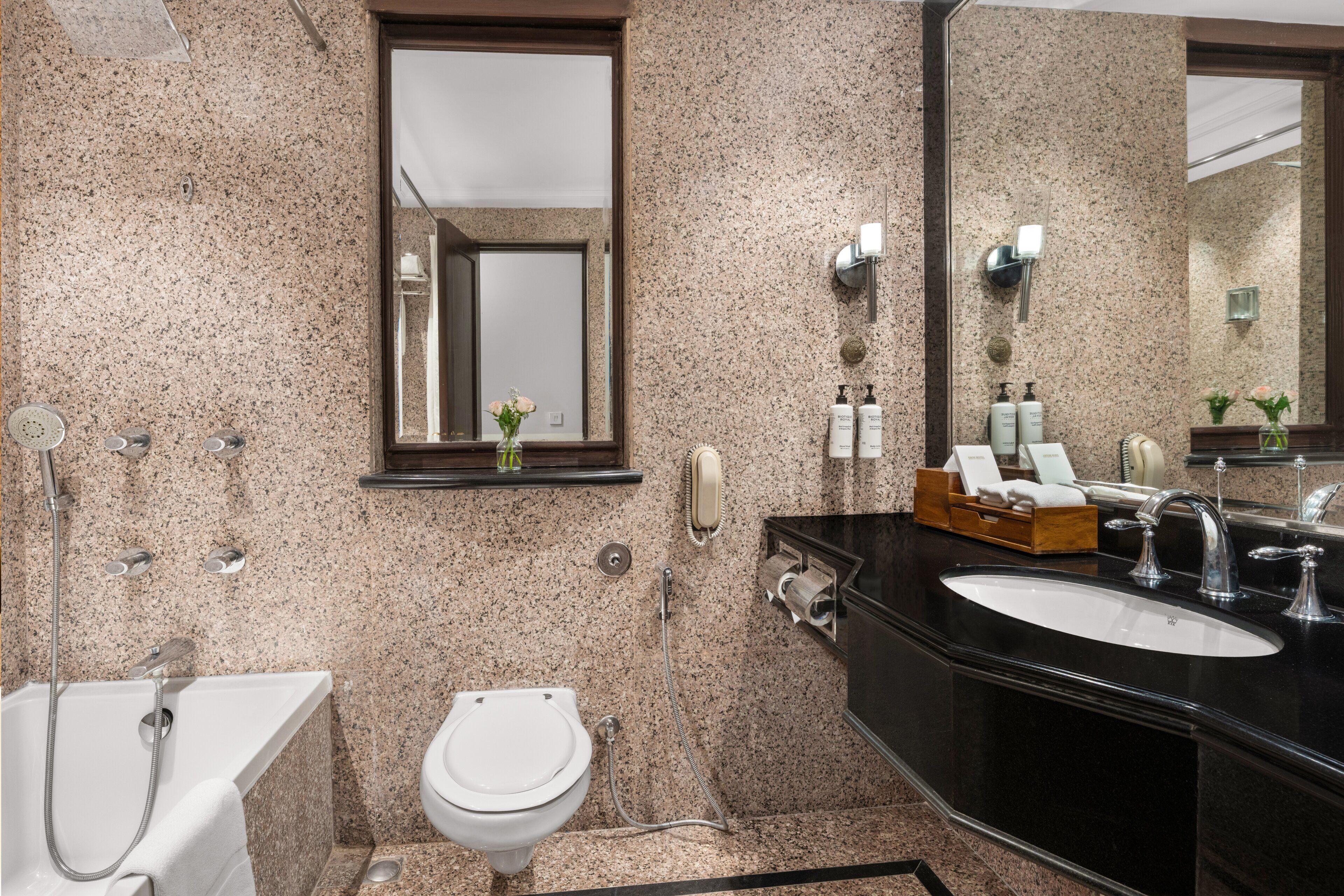Un baño con encimera de granito, inodoro blanco, bañera y espejo grande.