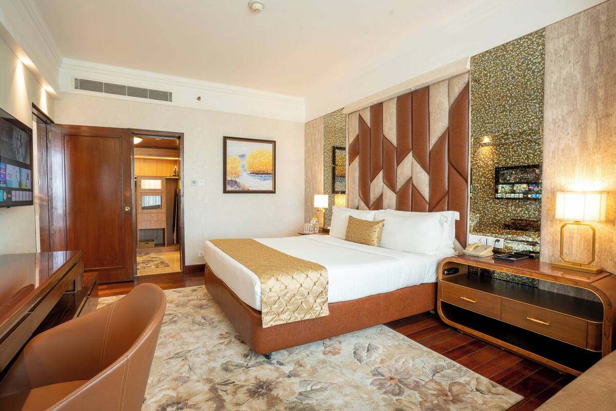 A hotel room with a bed, a desk, a chair, a TV, and a bathroom visible through an open door.