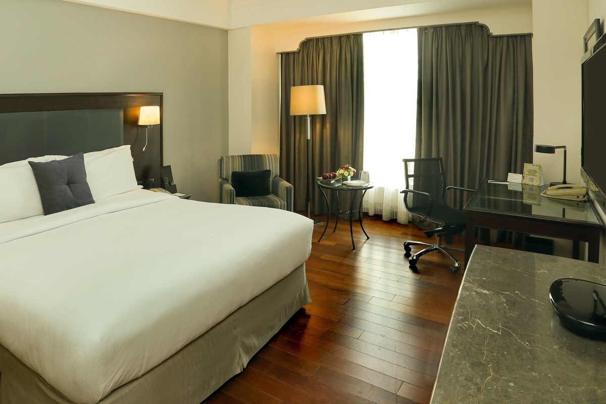 Une chambre d’hôtel avec un grand lit, un bureau, une chaise, une lampe et un téléviseur.