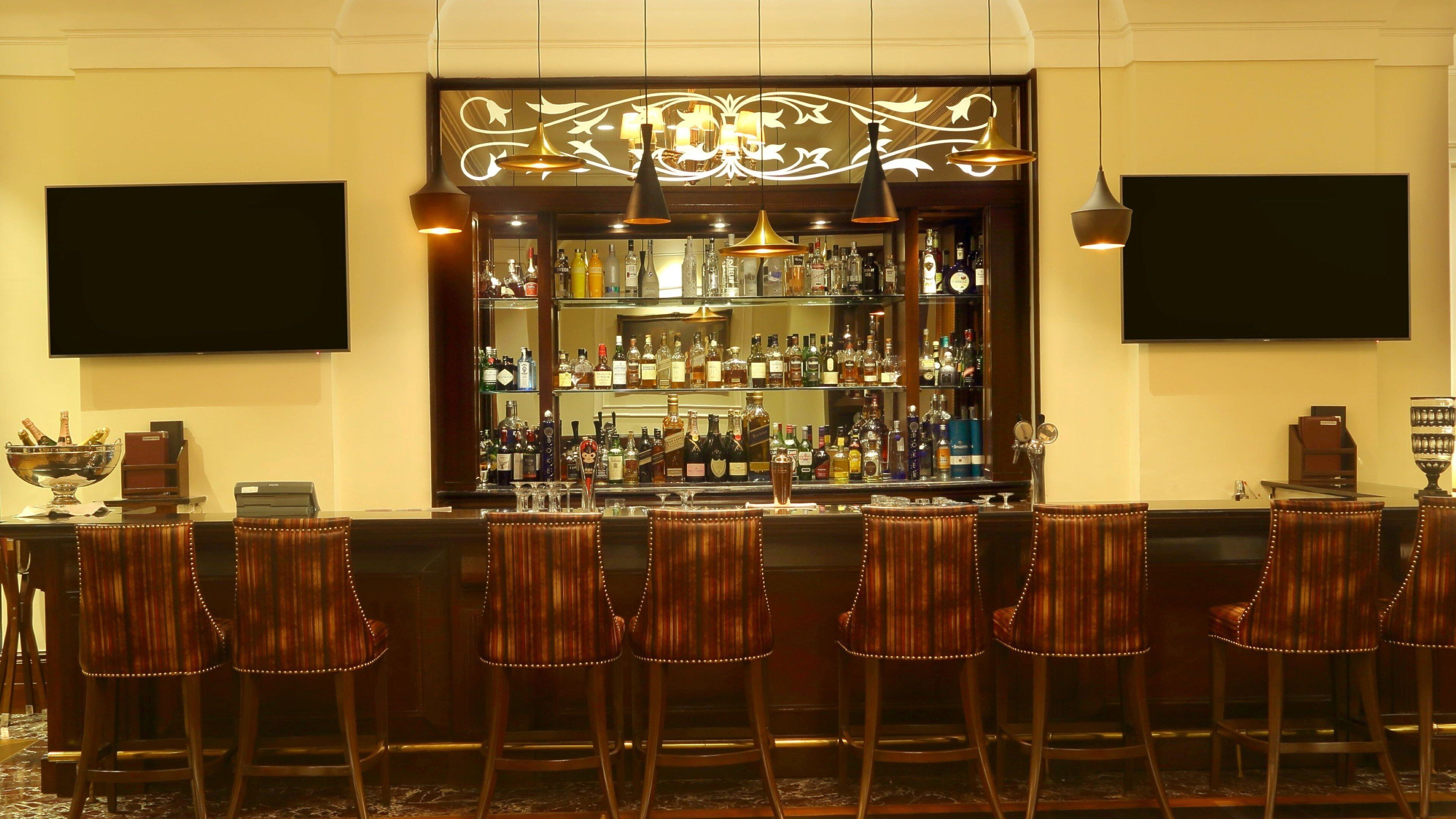 A bar area with a variety of liquor bottles, a bar counter, and several bar stools.