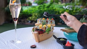A table with a glass of wine, sushi, and chopsticks.