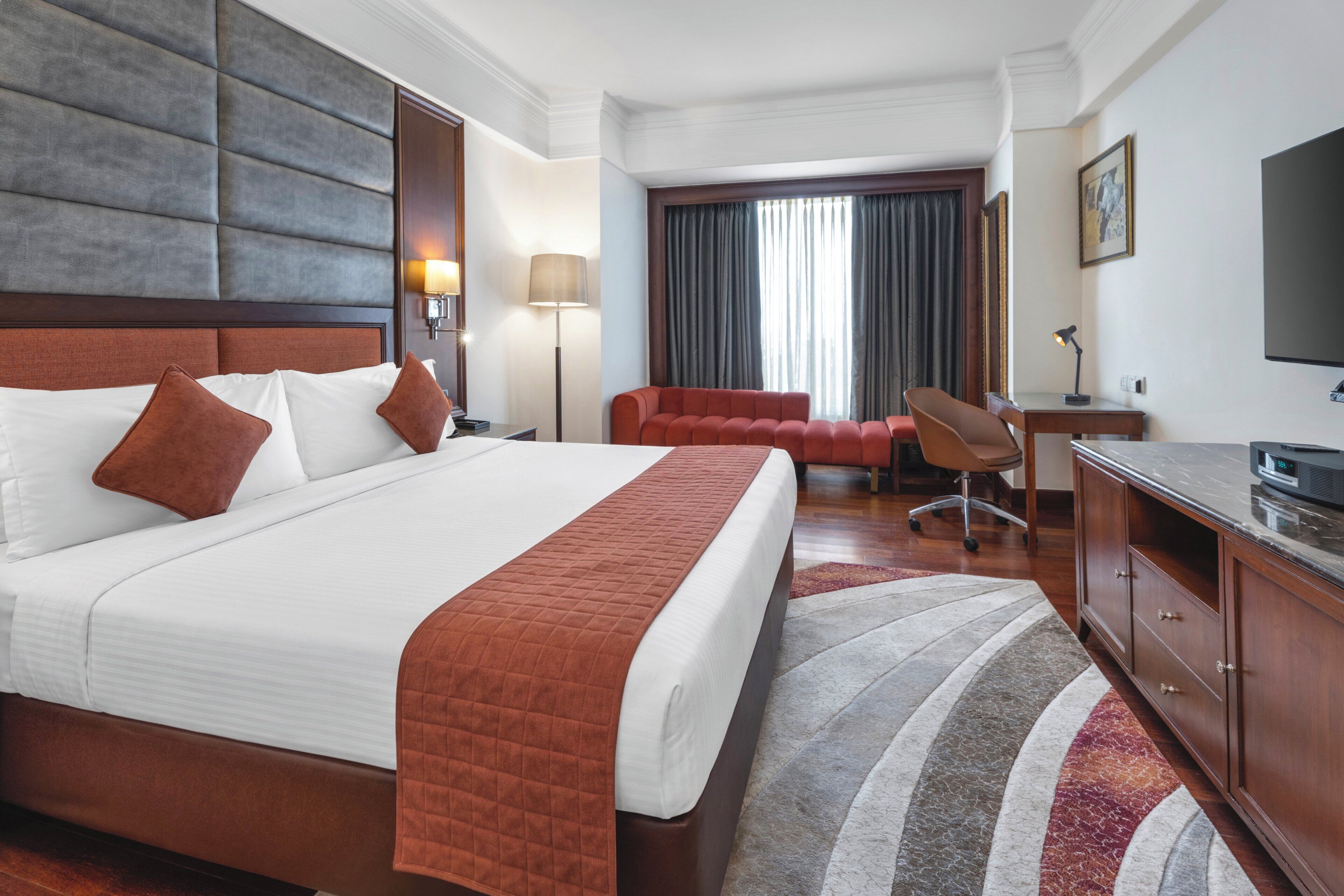 Una habitación de hotel con una cama grande, un escritorio, una silla, un televisor y una ventana con cortinas.
