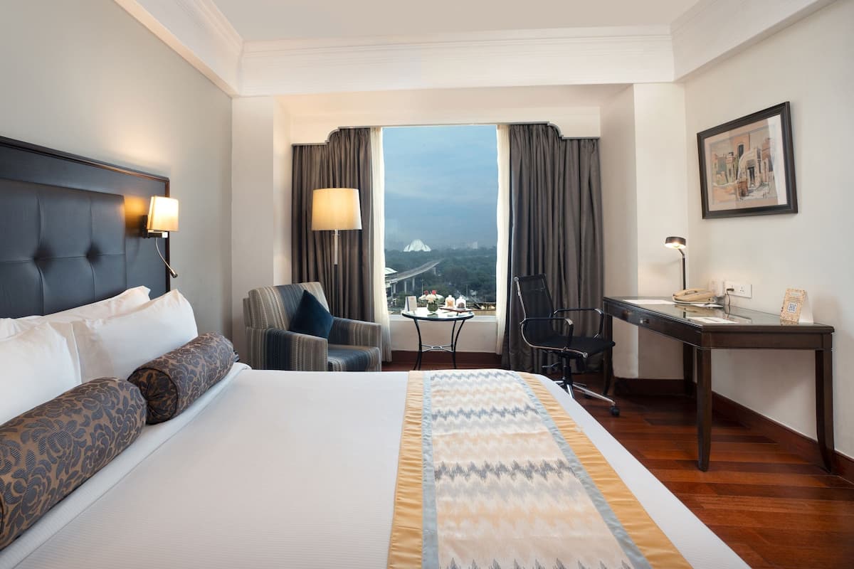 A hotel room with a large bed, a desk, a chair, and a view of a bridge.