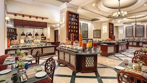 A hotel dining area with multiple seating arrangements, a buffet setup, and a kitchen in the background. - Eros Hotel New Delhi by IHG (New Delhi)
