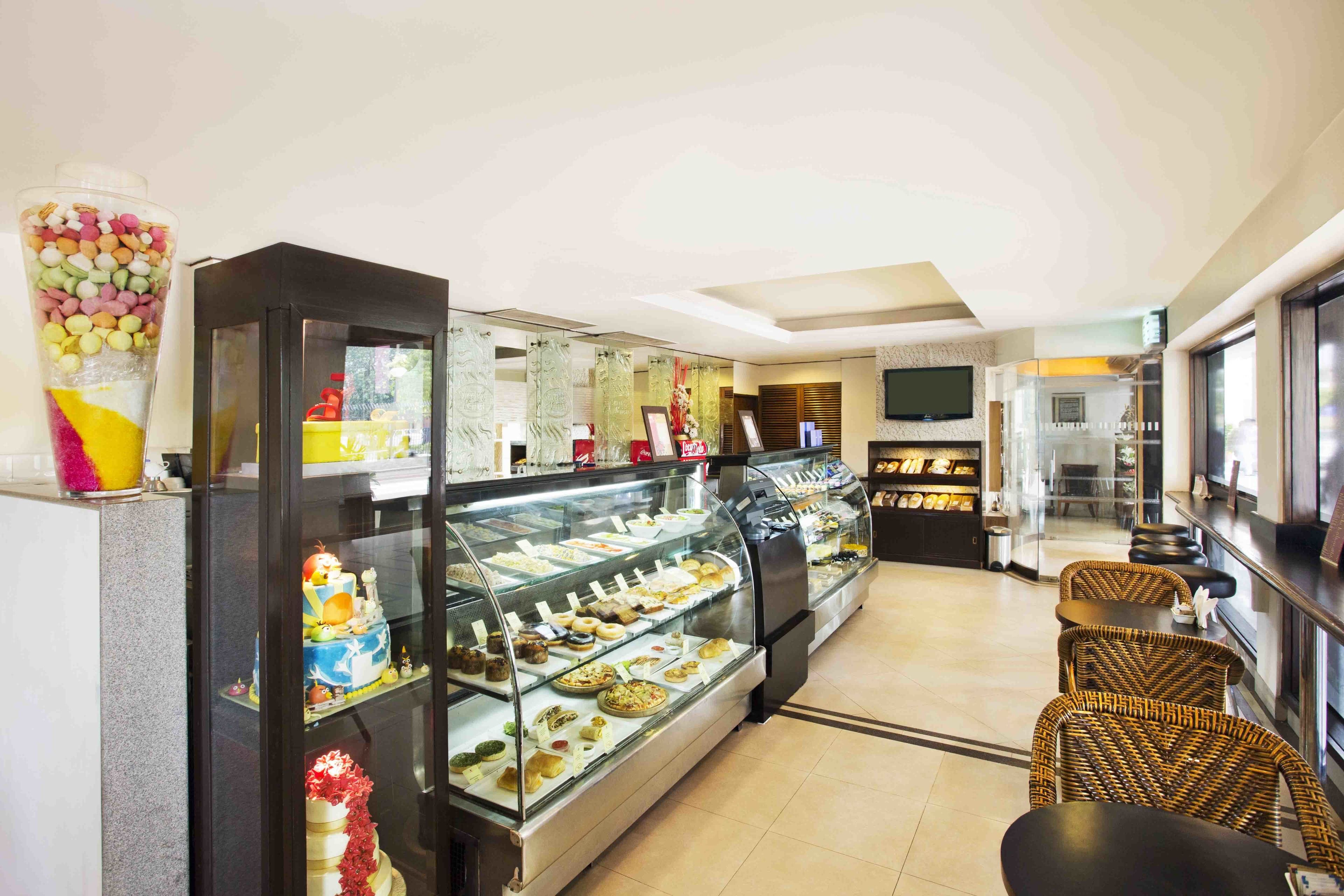 Une vitrine remplie de diverses pâtisseries, un coin salon avec des chaises en osier et un téléviseur fixé au mur.