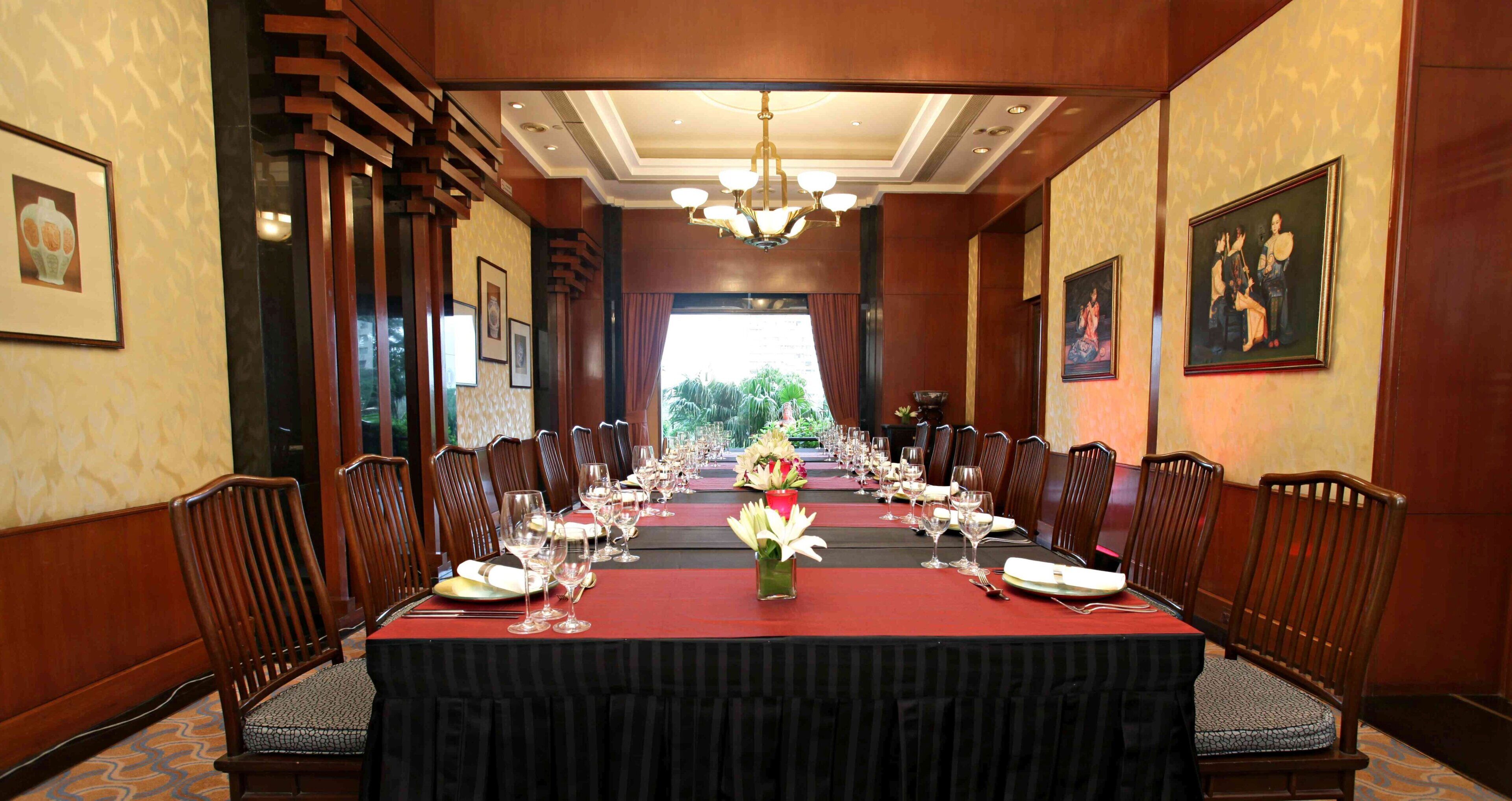 A formal dining room with a long table set for a meal, flanked by chairs, and a chandelier above.