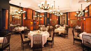 Une salle à manger d’hôtel avec de nombreuses tables rondes, des chaises et des lustres.