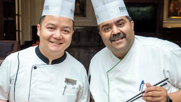 Two chefs in white uniforms holding plates of food.