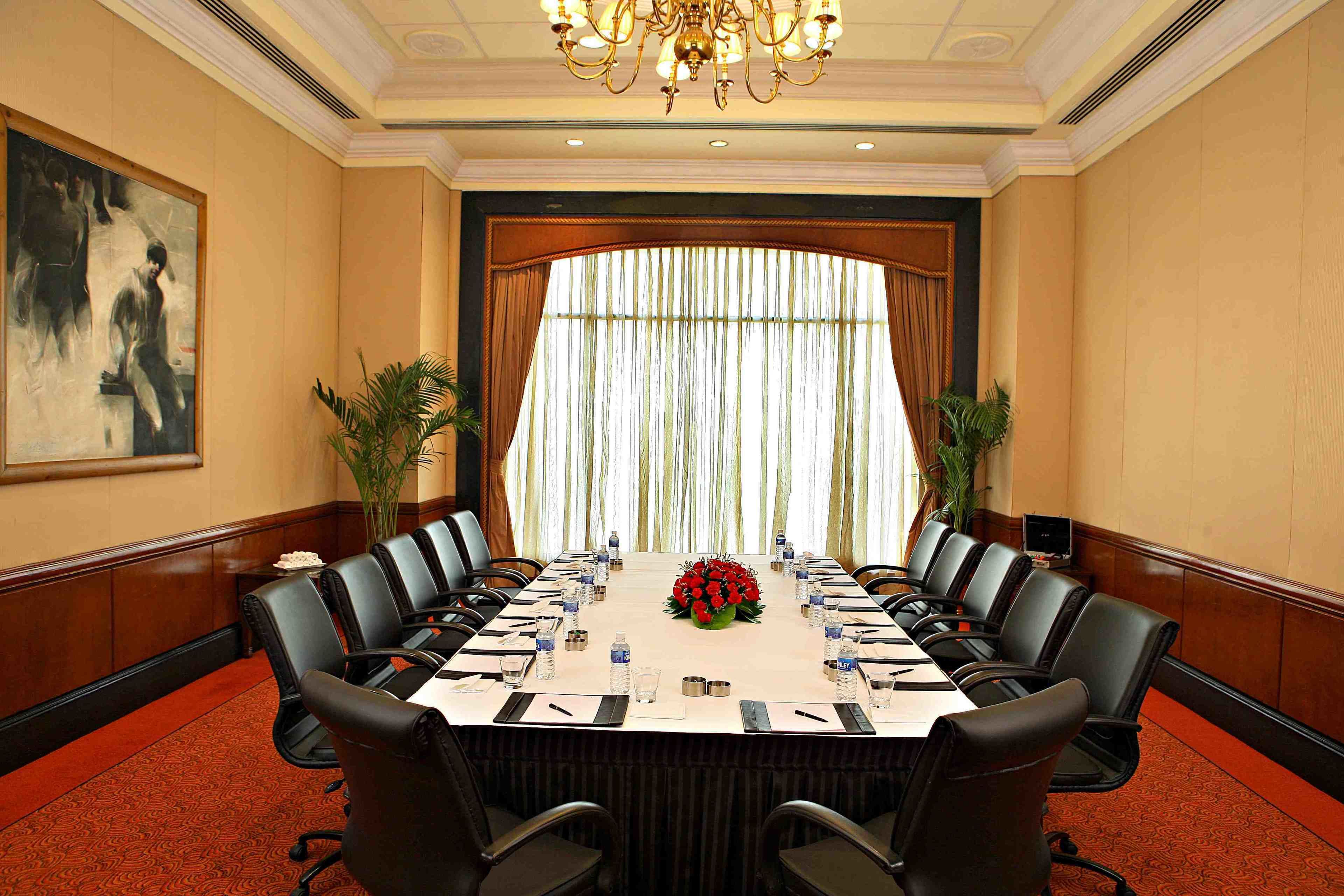 Ein Konferenzraum mit langem Tisch, mehreren Stühlen und einer Chandelüster.