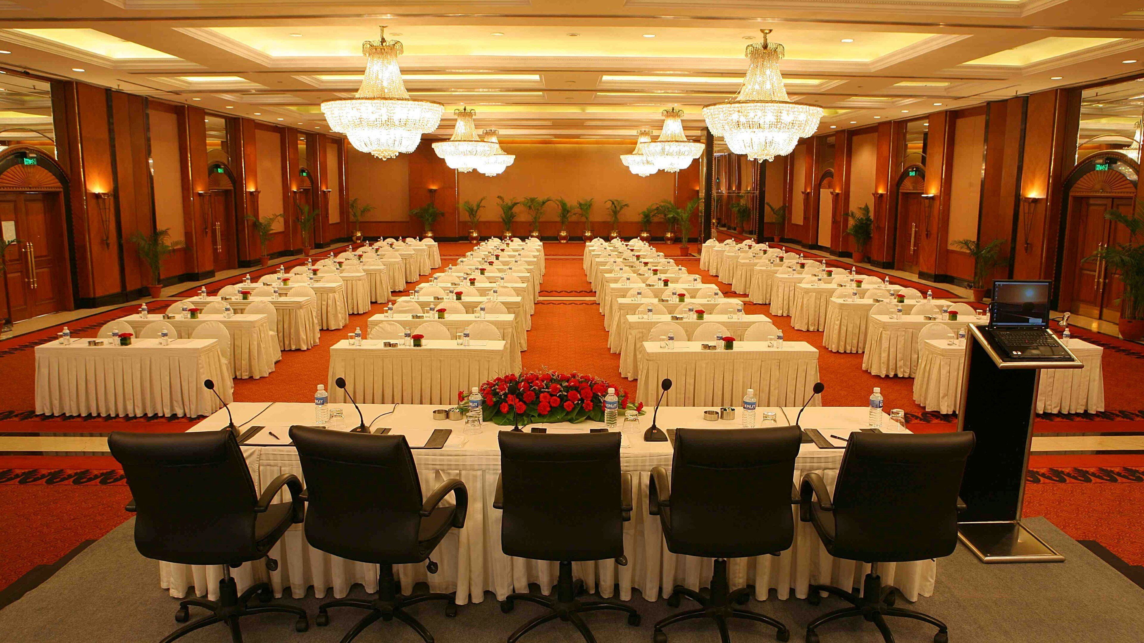 Un salón de conferencias con filas de mesas, sillas y un atril con una computadora portátil.