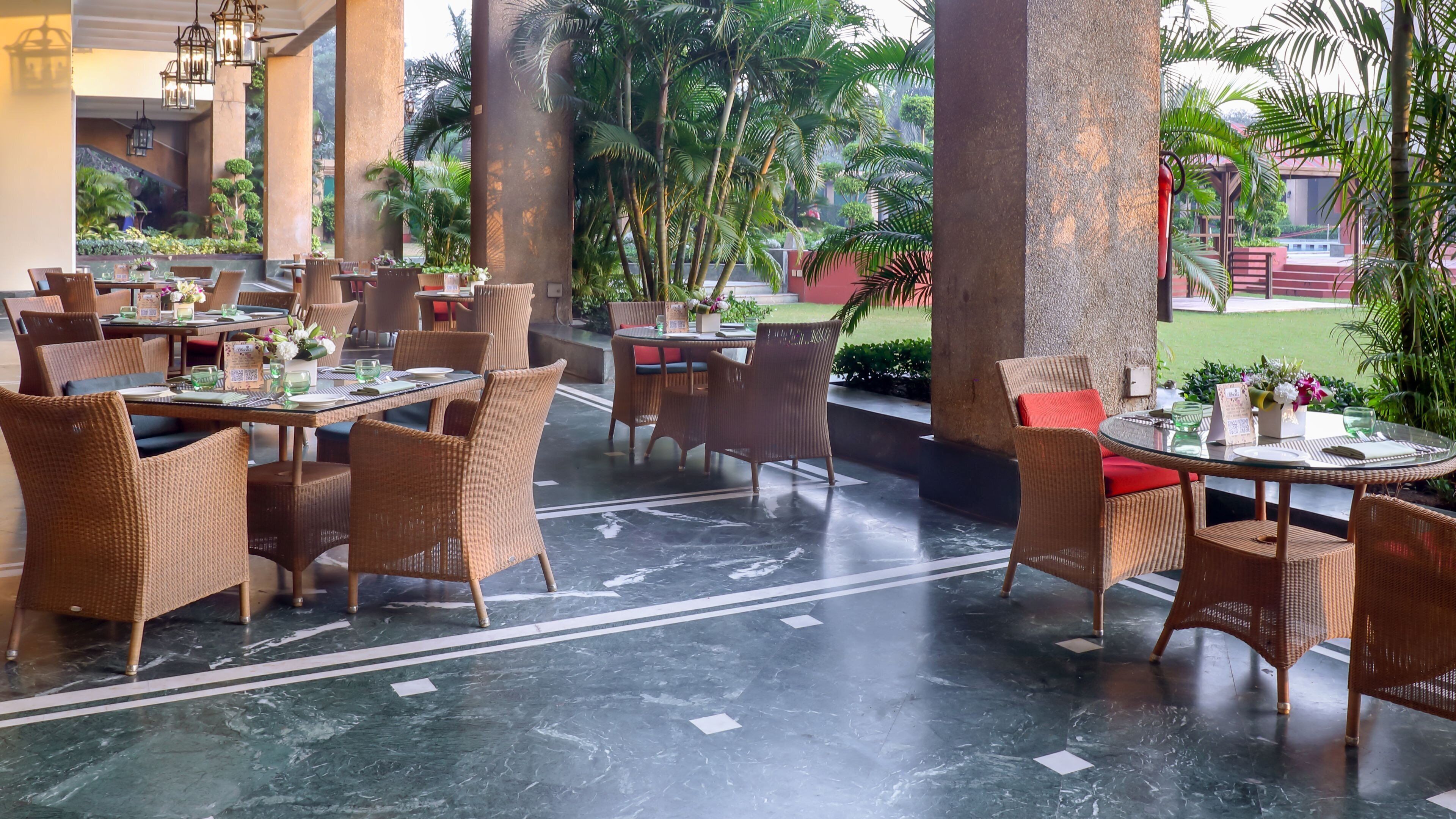 A restaurant with wicker furniture, marble flooring, and a view of greenery.