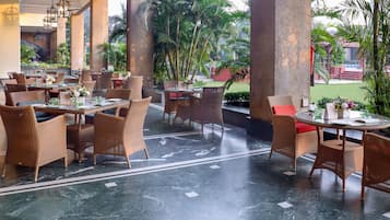 A restaurant with wicker furniture, marble flooring, and a view of greenery.