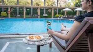 A woman relaxing by a poolside table with a plate of food and a drink, overlooking a swimming pool with lounge chairs and umbrellas in the background. - Eros Hotel New Delhi by IHG (New Delhi)