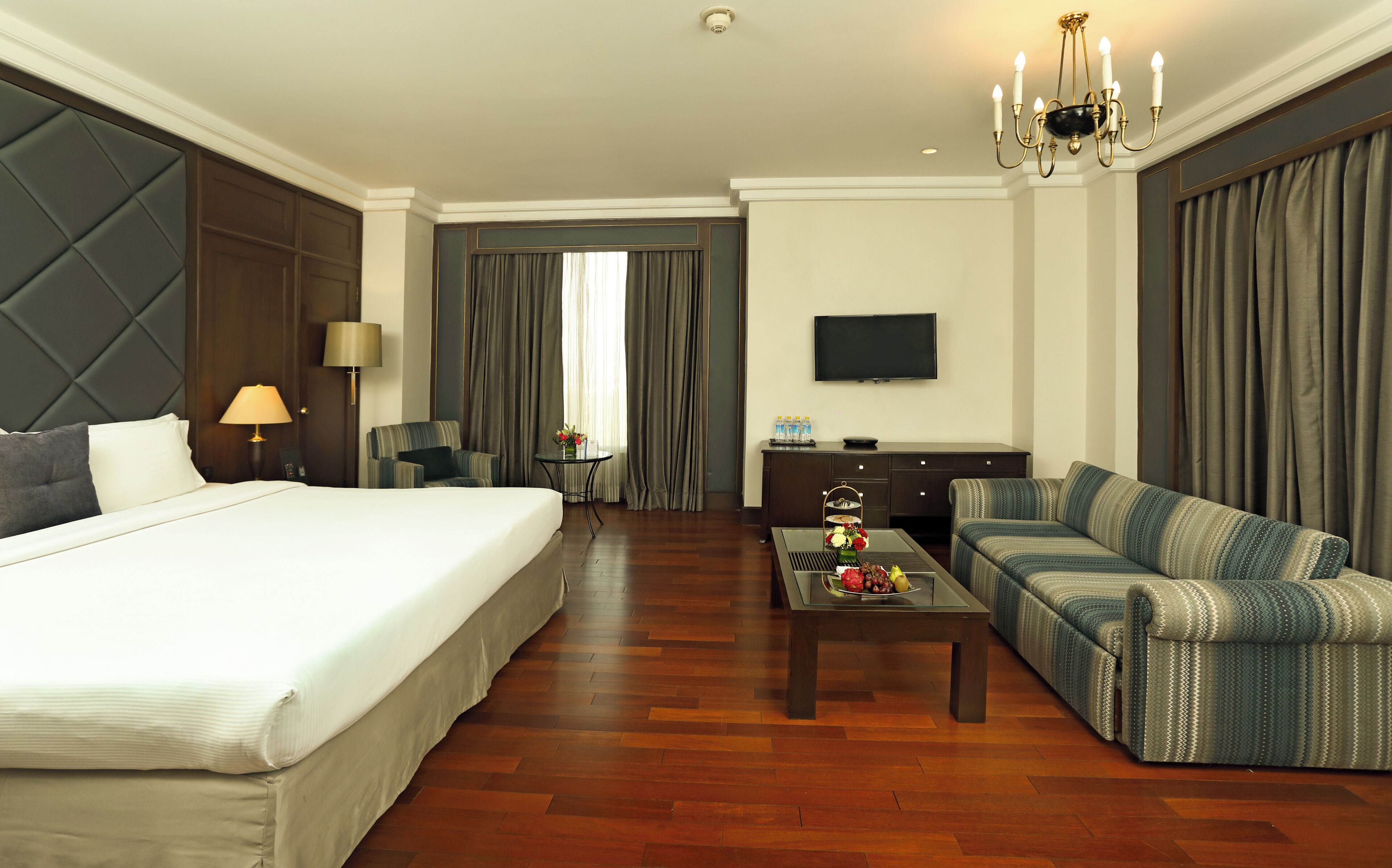 A hotel room with a large bed, a sofa, a coffee table, a TV, and a desk.