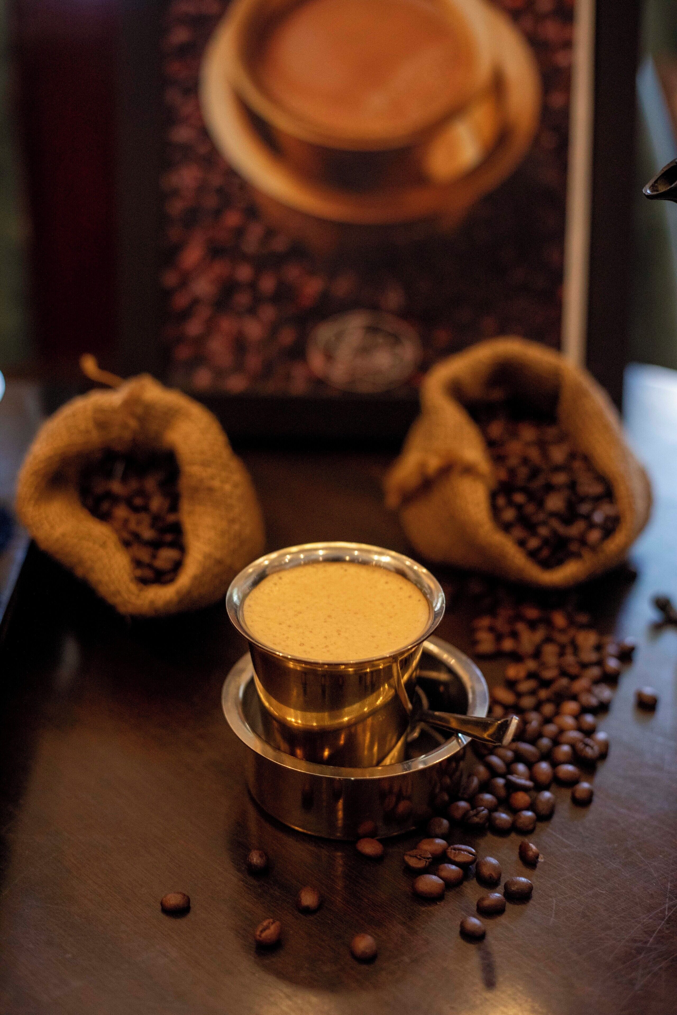 A coffee machine with a cup of coffee, two burlap sacks filled with coffee beans, and scattered coffee beans on a table.