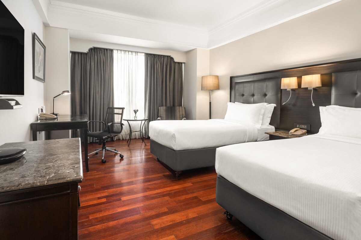 Une chambre d’hôtel avec deux lits, un bureau, une chaise, une lampe et un téléviseur.