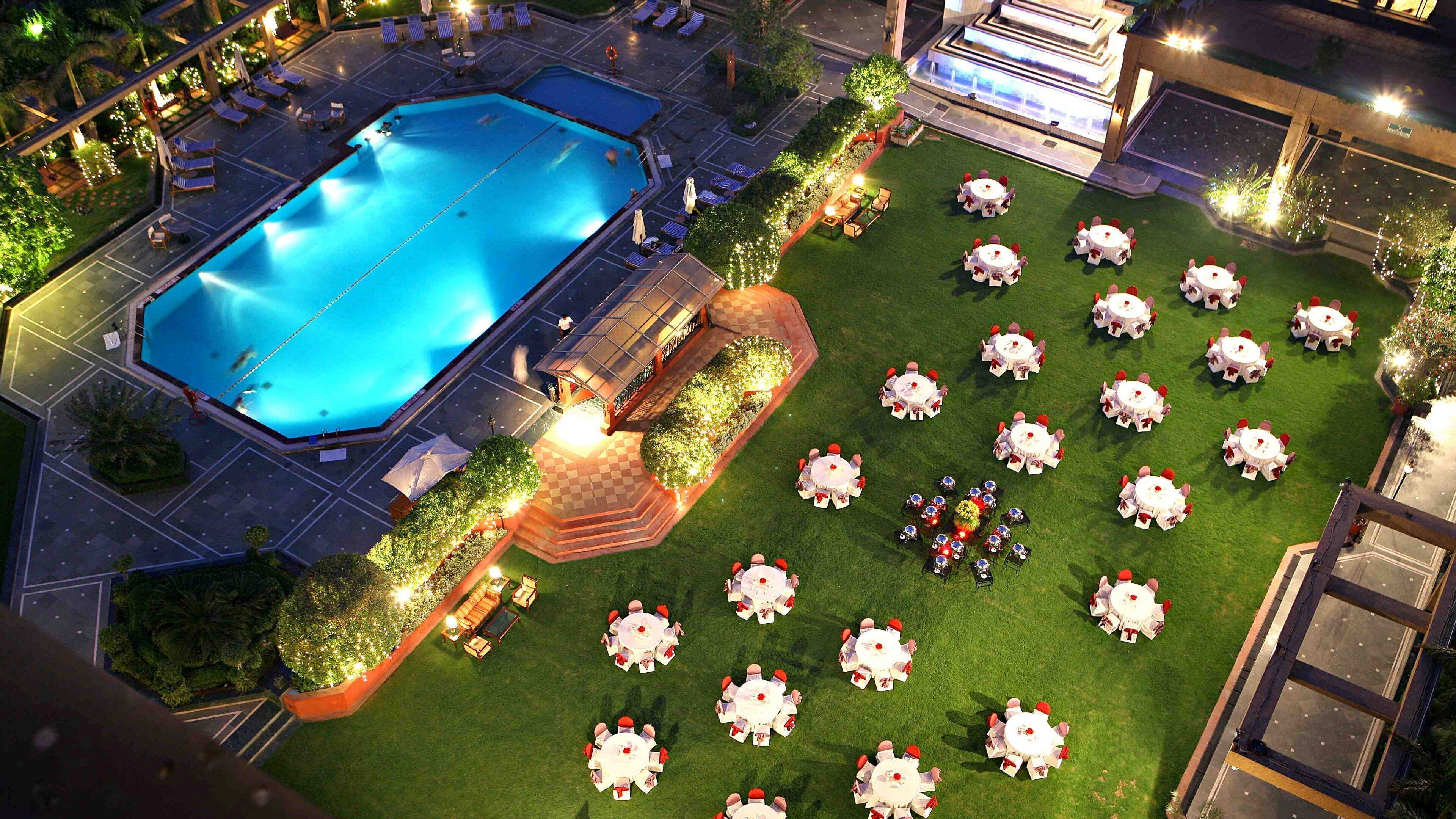 A rooftop pool with lounge chairs and tables, surrounded by a well-maintained lawn and a building with a modern design.