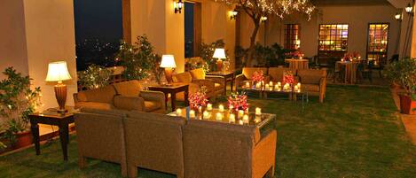 An outdoor seating area with sofas, tables, and candles. There are potted plants and a tree with lights.