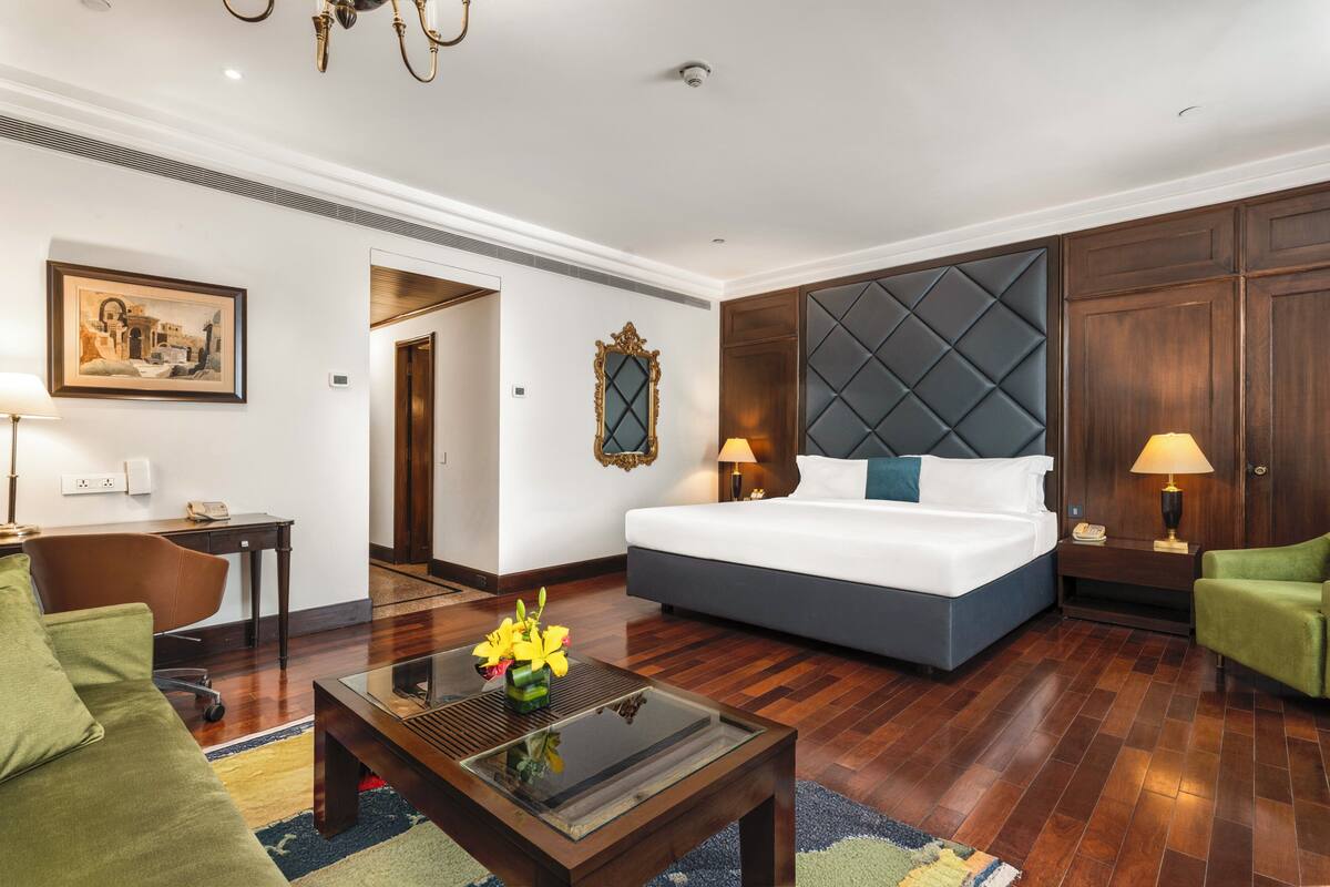 A hotel room with a bed, a desk, a chair, a coffee table, and a painting on the wall.