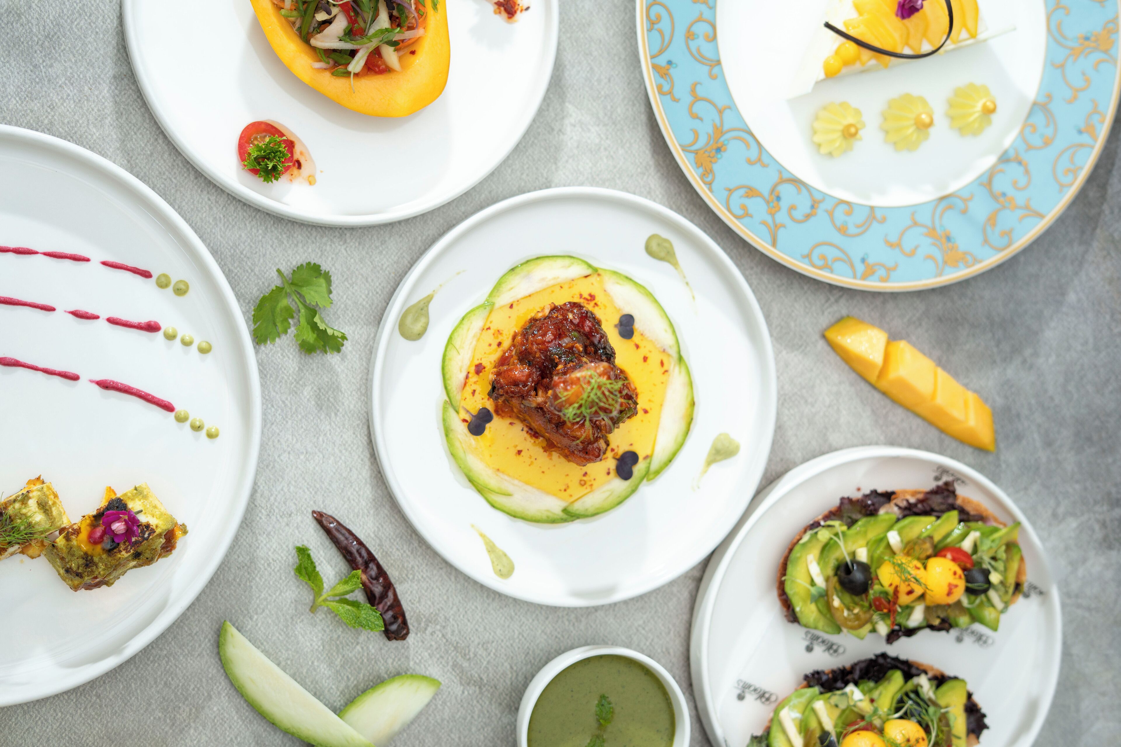 Une variété de plats présentés sur des assiettes, notamment des salades à base d’avocat et un plat de poivrons farcis.
