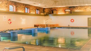 An indoor swimming pool with a tiled floor, a stone wall, and a wooden deck. - Talbot Hotel Wexford (Wexford)