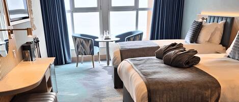 A hotel room with two beds, a desk, a chair, a small table, and a large window.