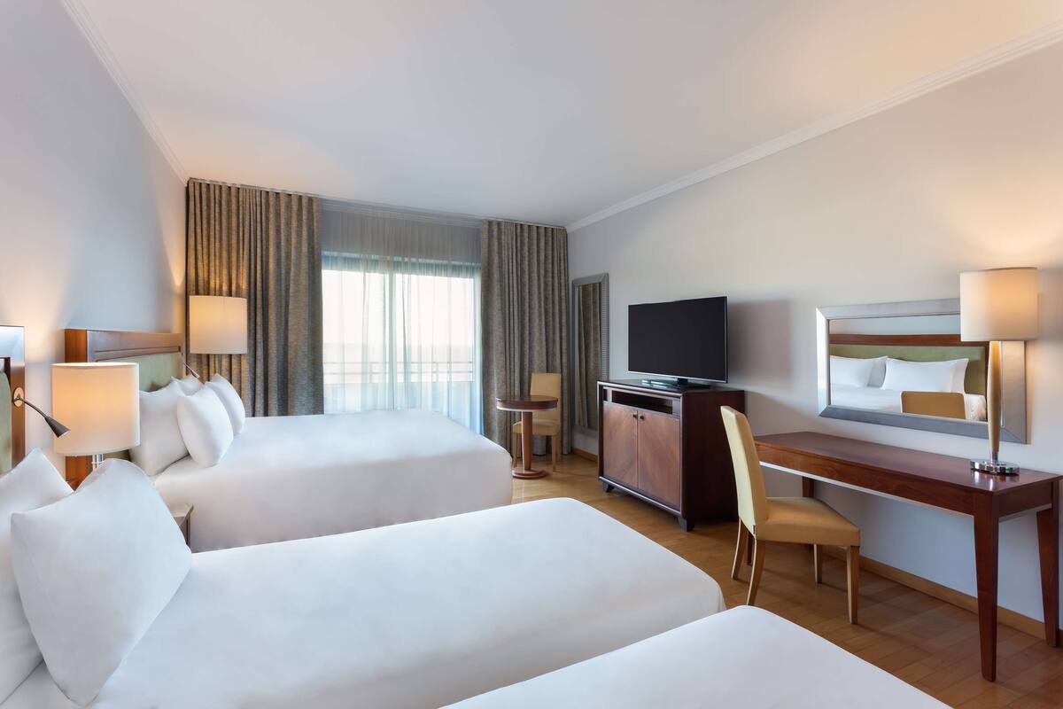 A hotel room with two beds, a desk, a TV, and a chair.