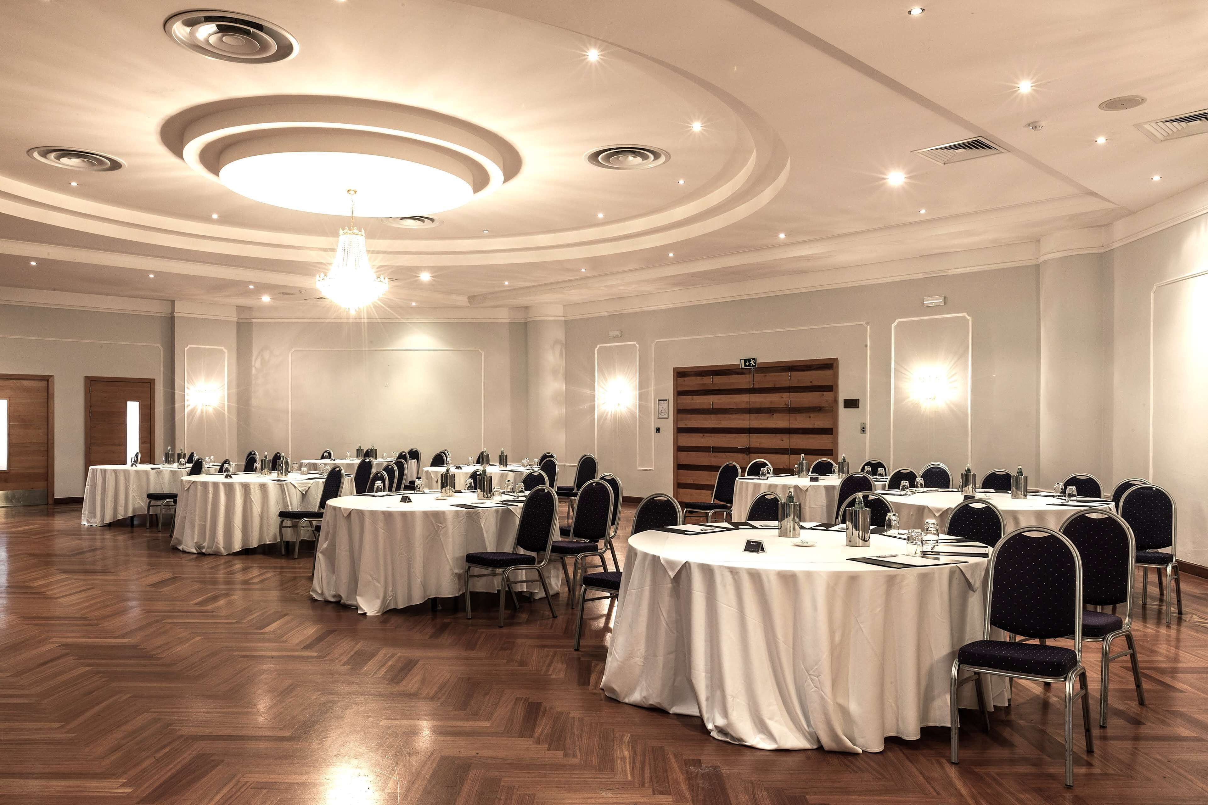 Una sala de conferencias con varias mesas redondas, cada una con sillas, equipada con botellas de agua y blocs de notas.