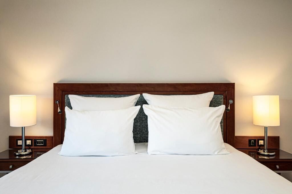 A neatly made bed with two pillows, a wooden headboard, and bedside lamps on either side.