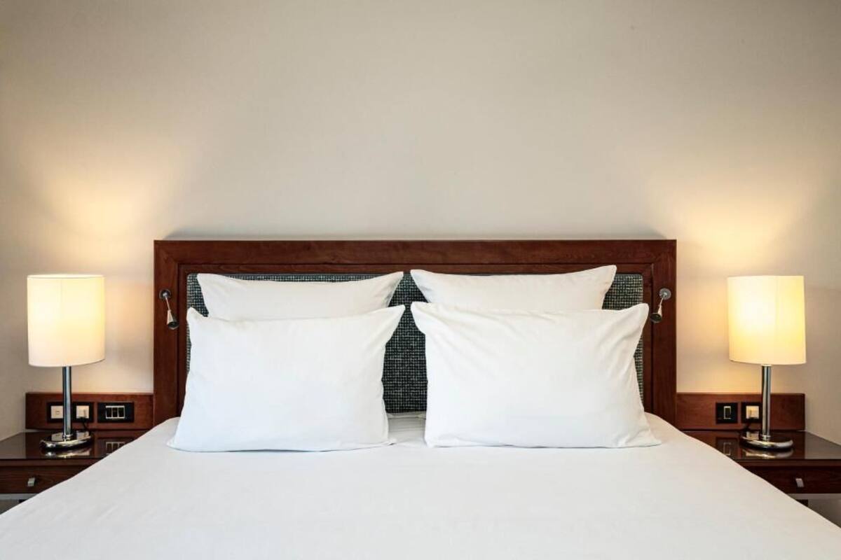 A neatly made bed with two pillows, a wooden headboard, and bedside lamps on either side.