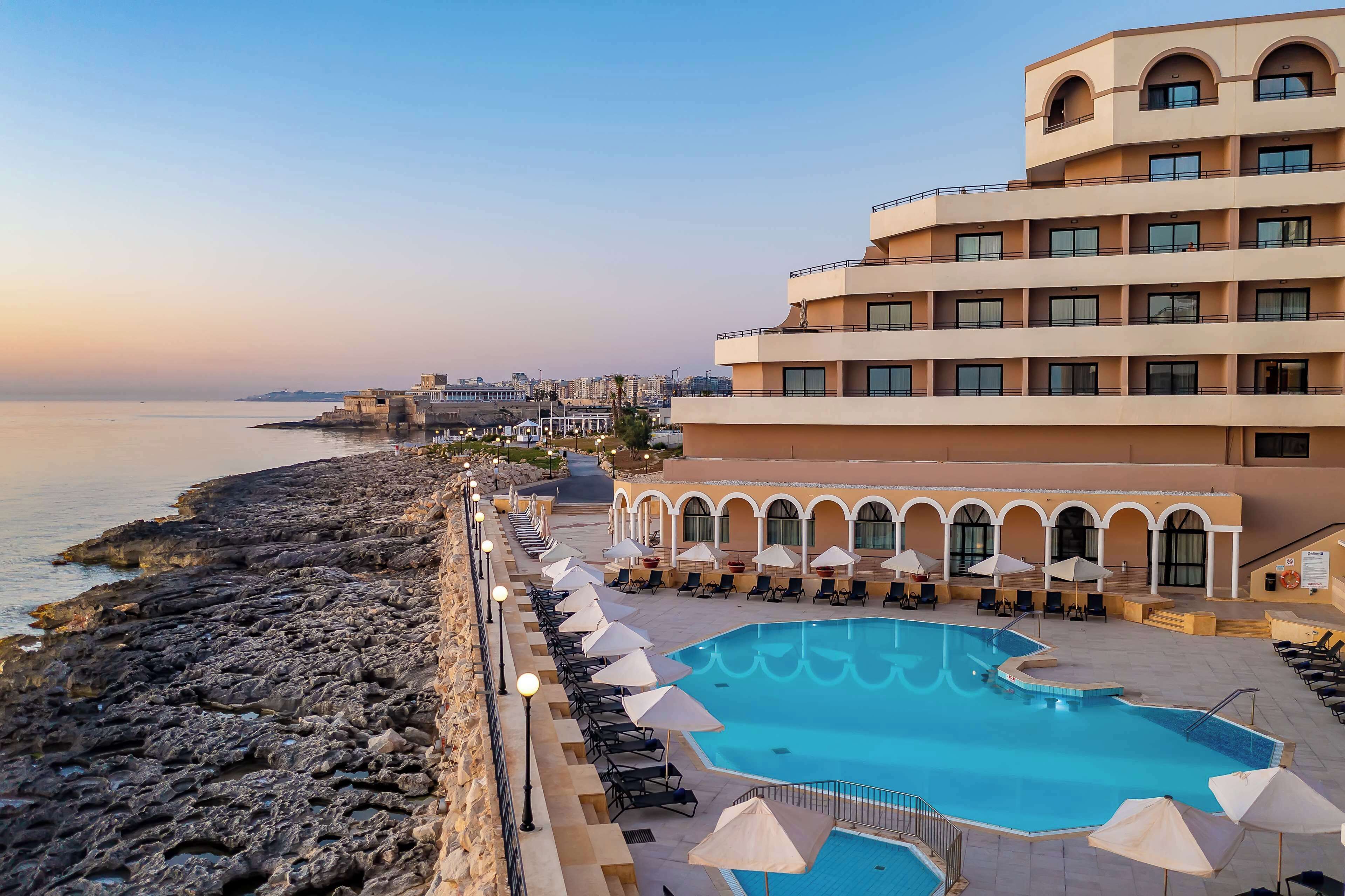 A resort with a pool, sun loungers, and a view of the sea.
