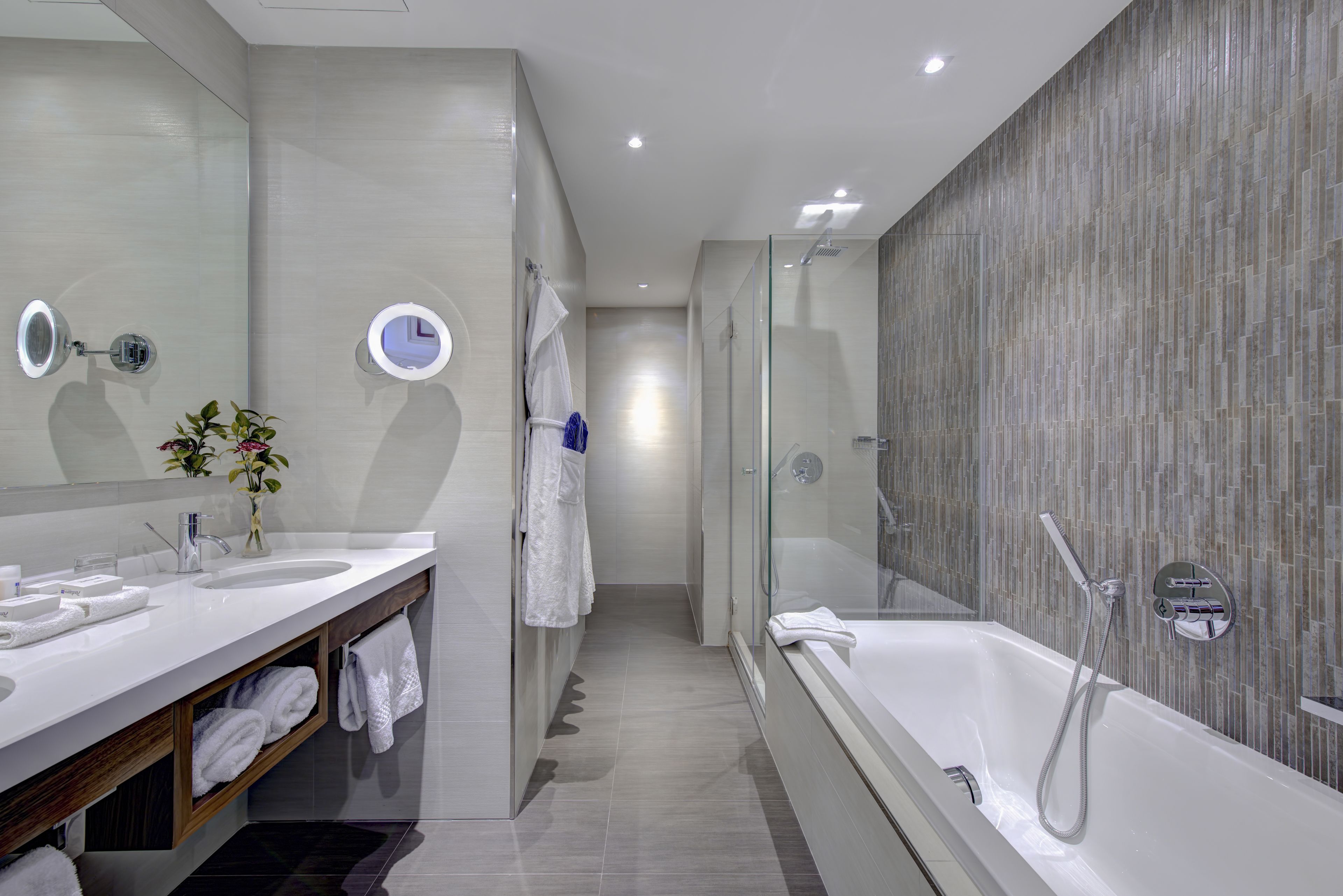 A modern bathroom with a large mirror, a bathtub, and a vanity with a sink and towel rack.