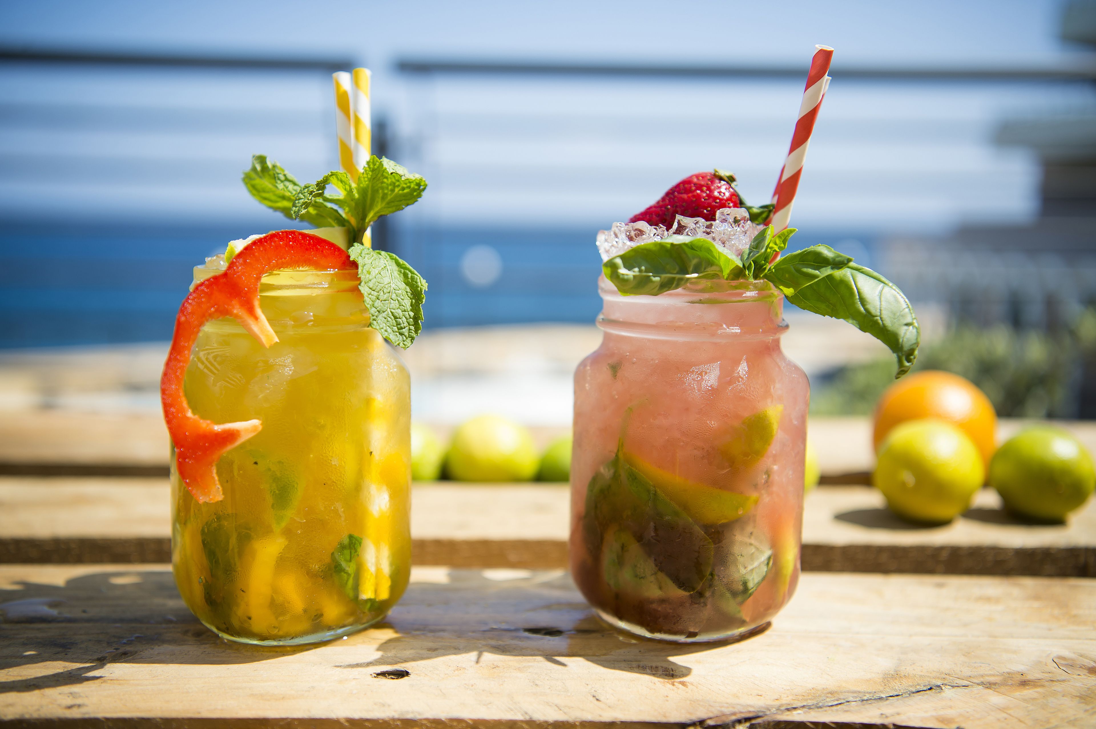 Two drinks on a wooden table with a view of the sea in the background.