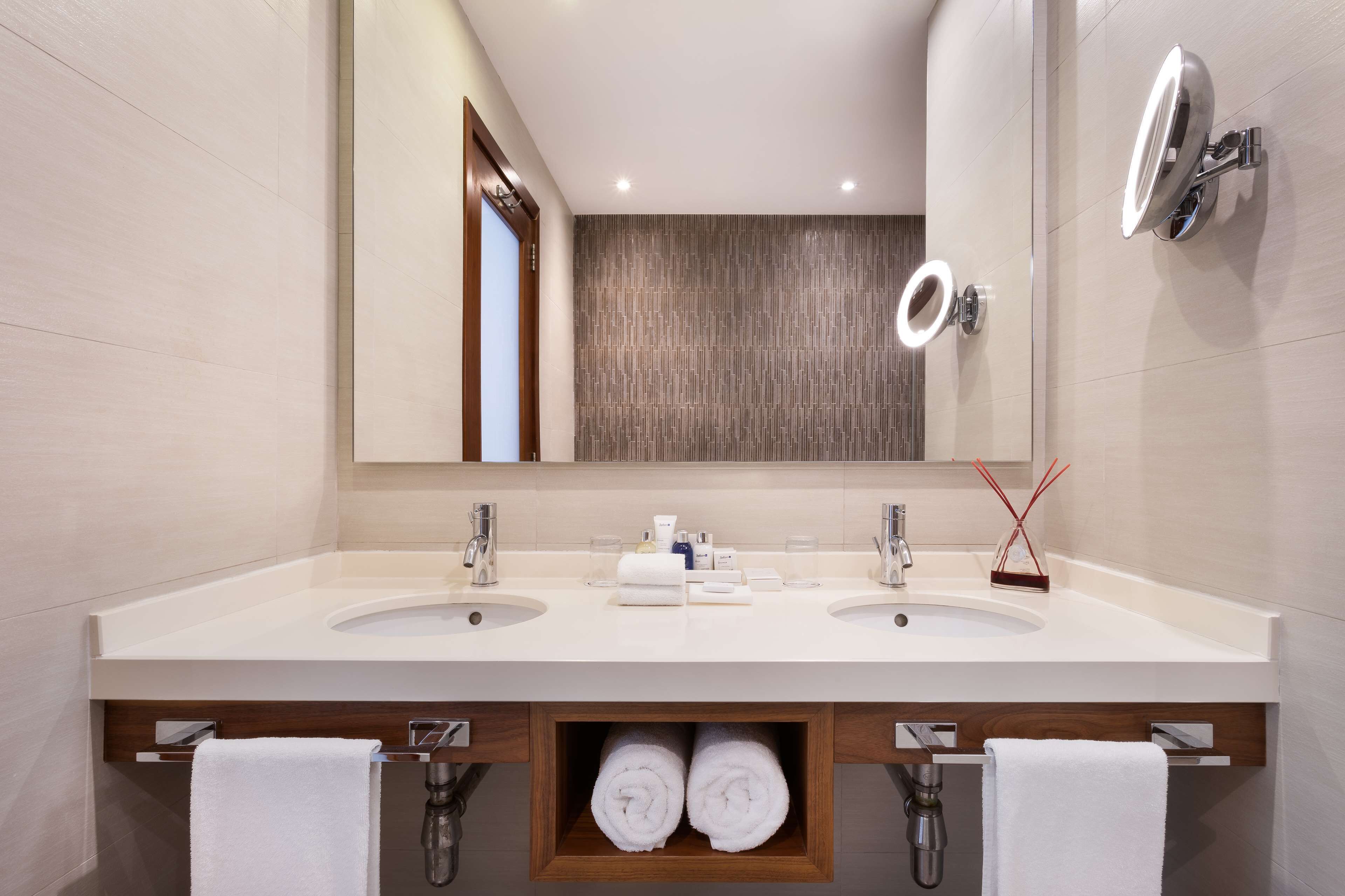 A modern bathroom with two sinks, a large mirror, and a towel rack.