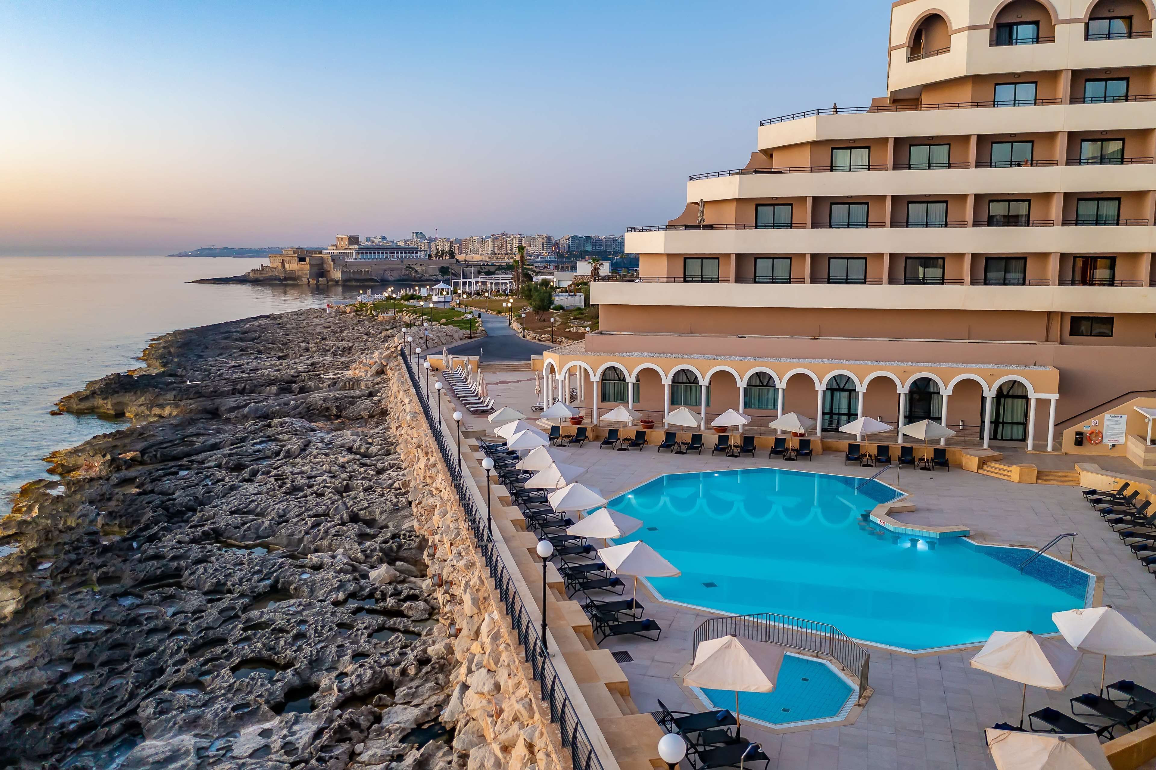 A resort with a large pool, lounge chairs, and a view of the sea.
