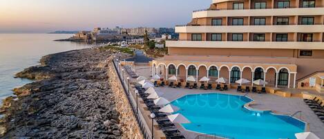 A resort with a large pool, lounge chairs, and a view of the sea.