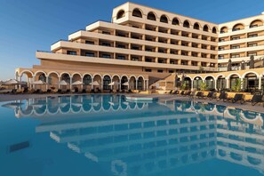 Un hotel con una piscina amplia, varios balcones y tumbonas.