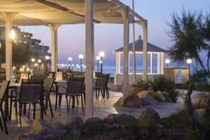 An outdoor dining area with tables and chairs, a covered seating area, and a view of the sea.