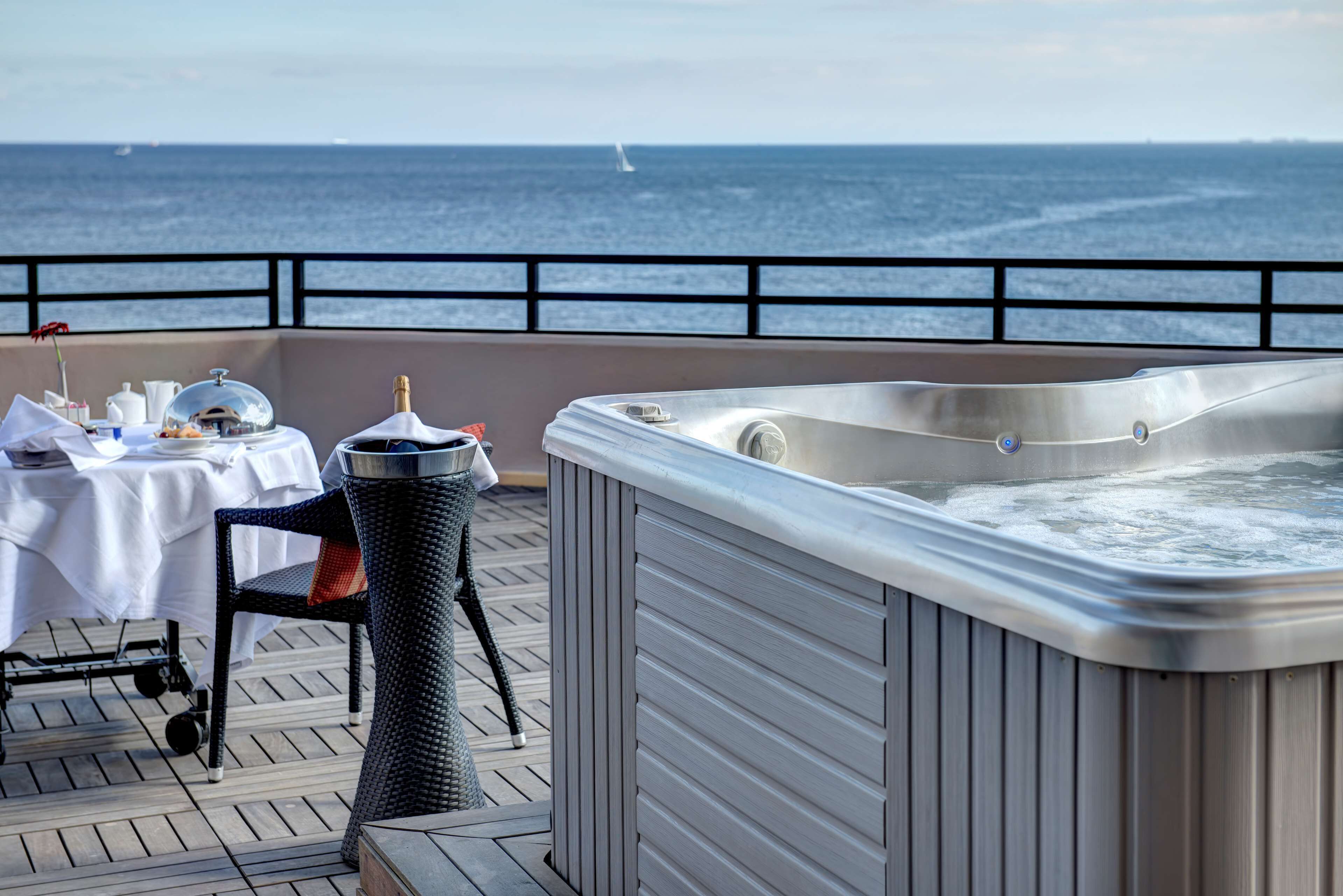 A hot tub on a deck with a table and chairs, overlooking the ocean.