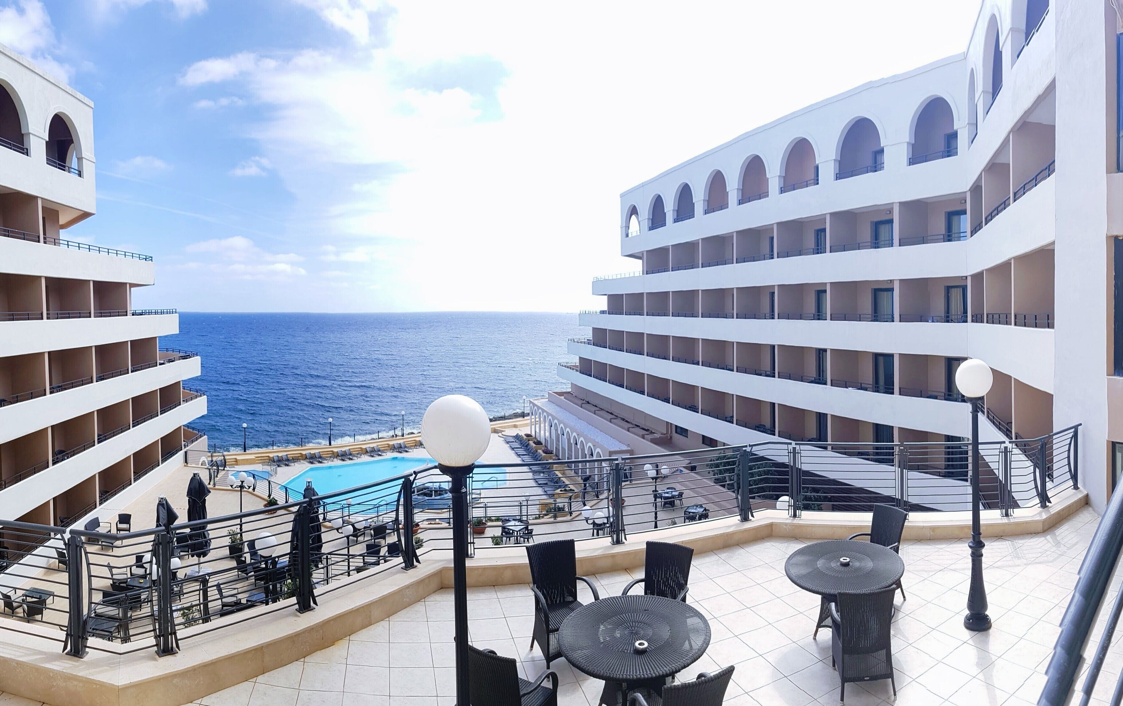 A hotel balcony with a pool, outdoor seating, and a view of the sea.