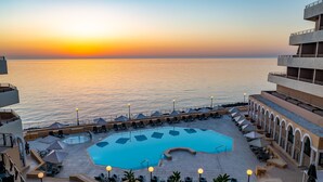 A rooftop pool area with a view of the sea at sunset, surrounded by lounge chairs and umbrellas. - Radisson Blu Resort, Malta St. Julian's (St. Julian's)
