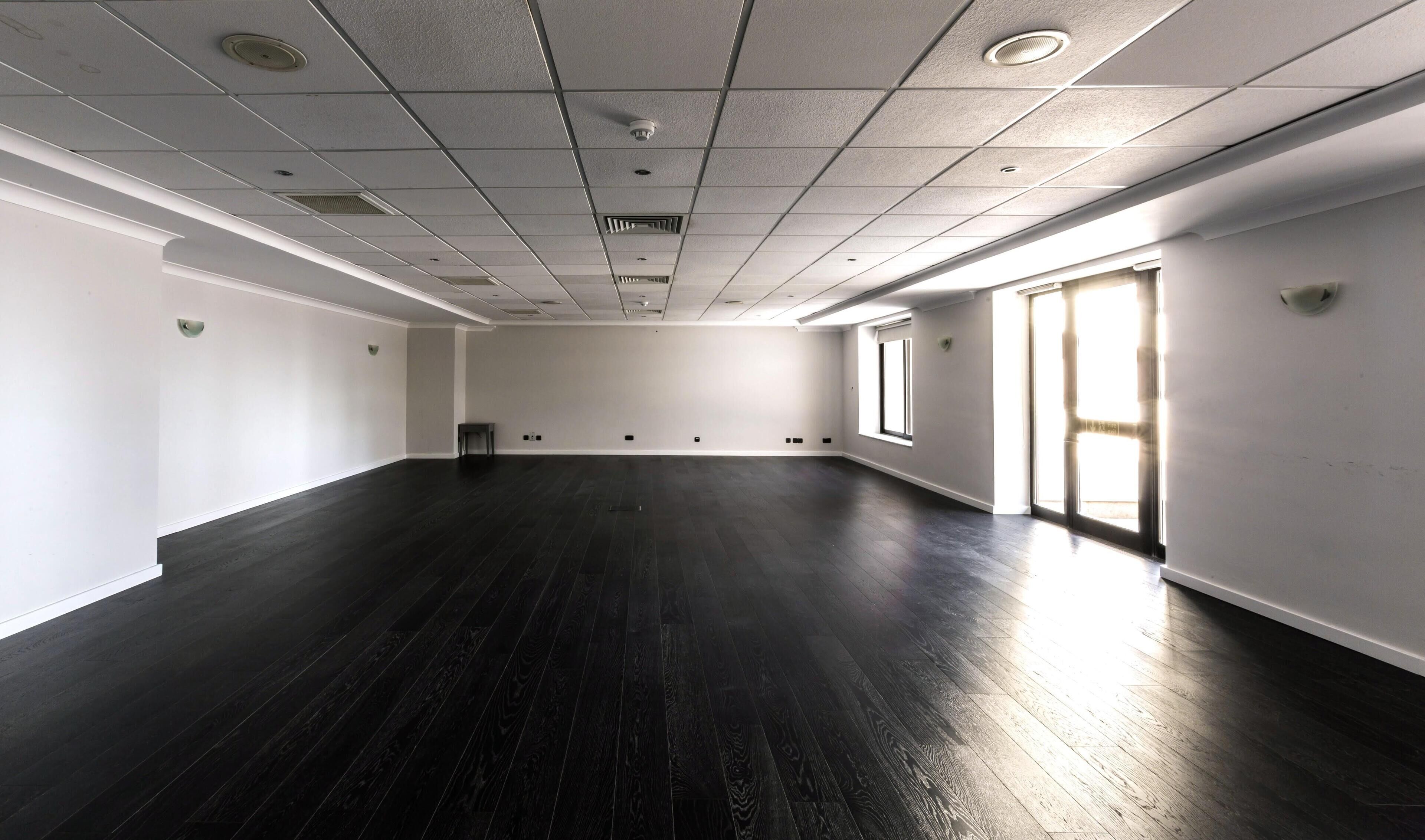 A large, empty room with dark wooden floors, white walls, and a high ceiling with recessed lighting.