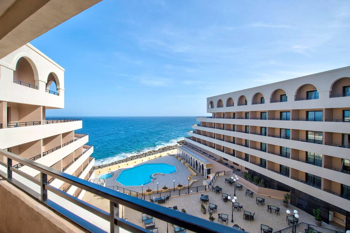 A hotel with multiple balconies overlooking a pool and the ocean.