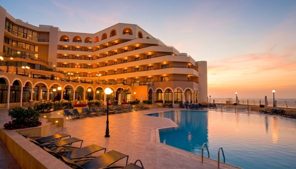 Un hotel con piscina, varios balcones y vista al atardecer.