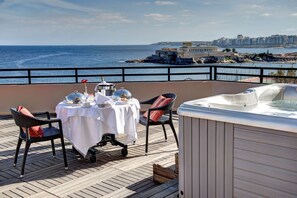 A balcony with a table set for two, overlooking a coastal cityscape.