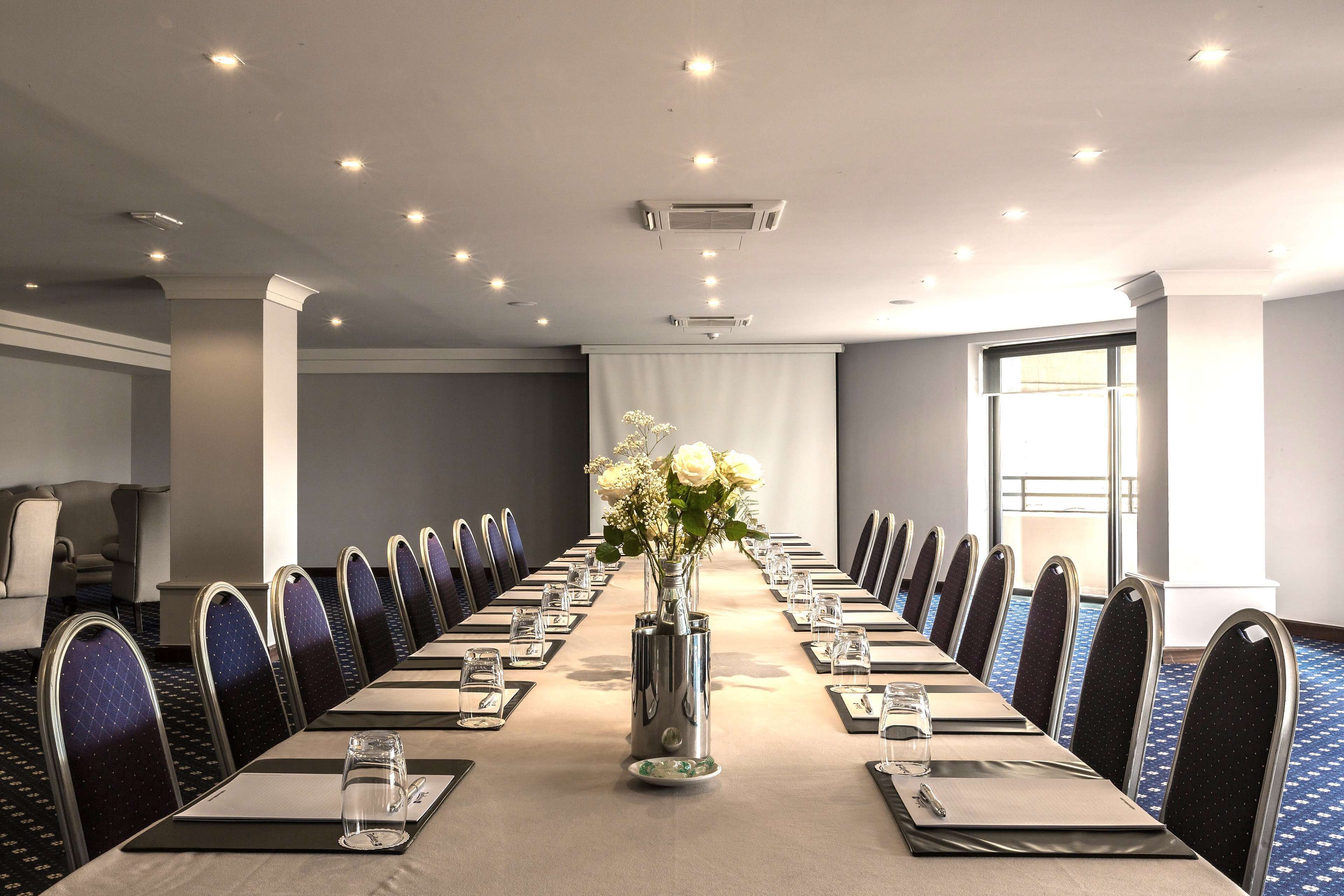 Een vergaderzaal met een lange tafel, stoelen en een bloevas.